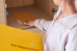 Person placing a yellow ExpressEnvelope into a wooden mail slot