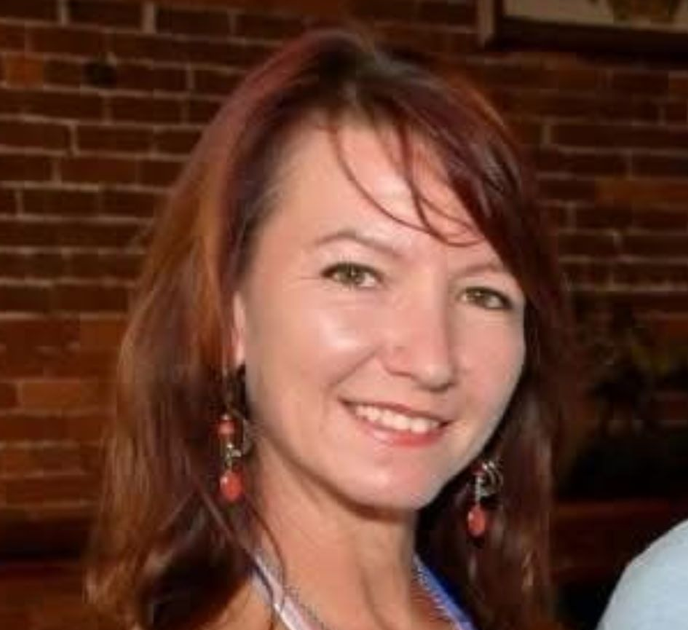 Headshot of a smiling woman in a white jacket and green blouse against a neutral background