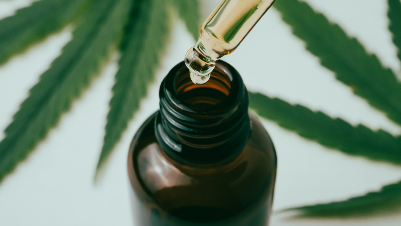 Brown dropper bottle with green cannabis leaves in the background and liquid being dispensed into it
