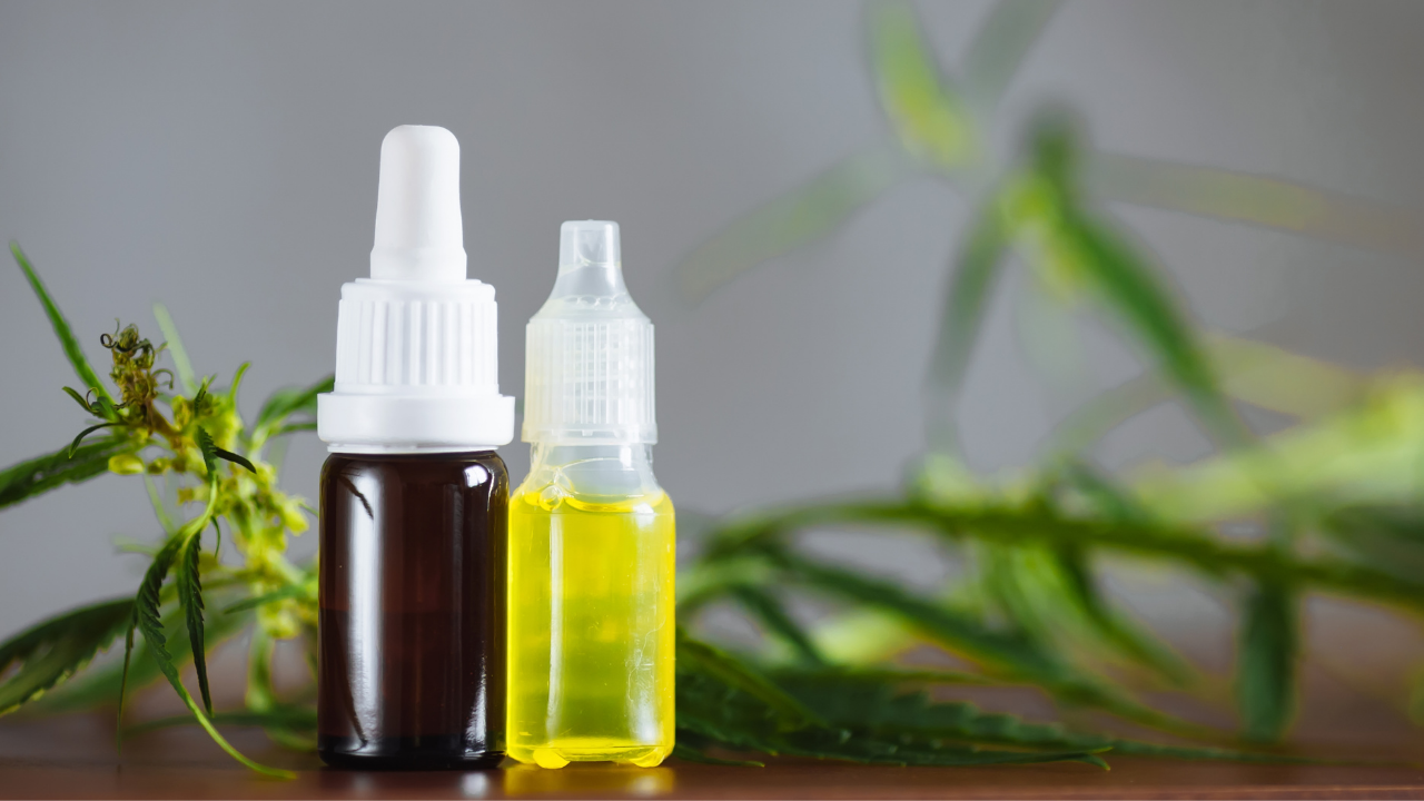 Two small dropper bottles, one amber and one clear yellow, on a wooden surface with green leaves.