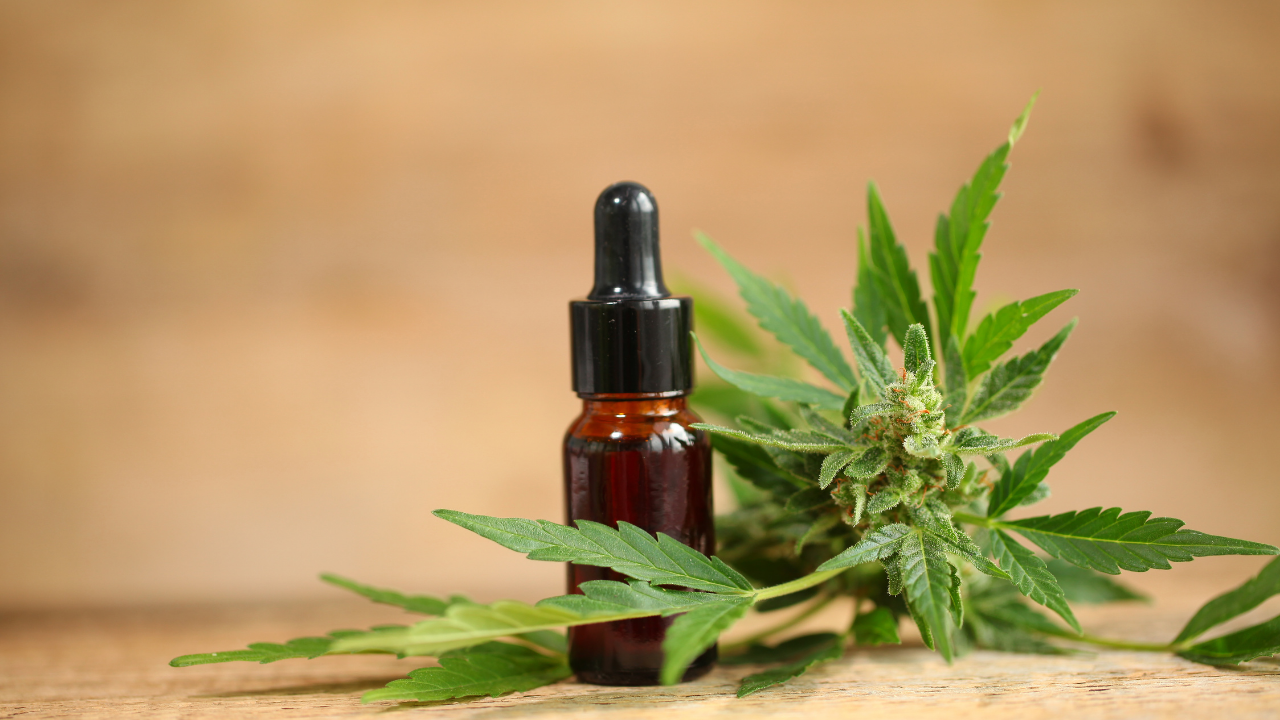 Brown dropper bottle with cannabis buds and green leaves on a wooden surface
