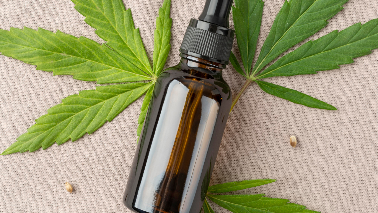 Amber dropper bottle surrounded by green cannabis leaves on a beige fabric background