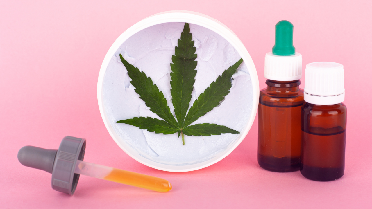 Cannabis leaf on a plate with droppers and medicine bottles on a pink background