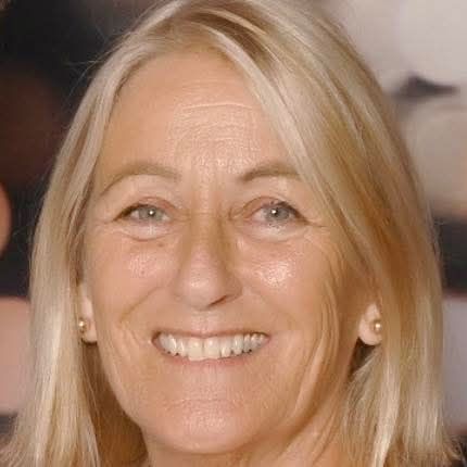 Headshot of a smiling woman in a white jacket and green blouse against a neutral background