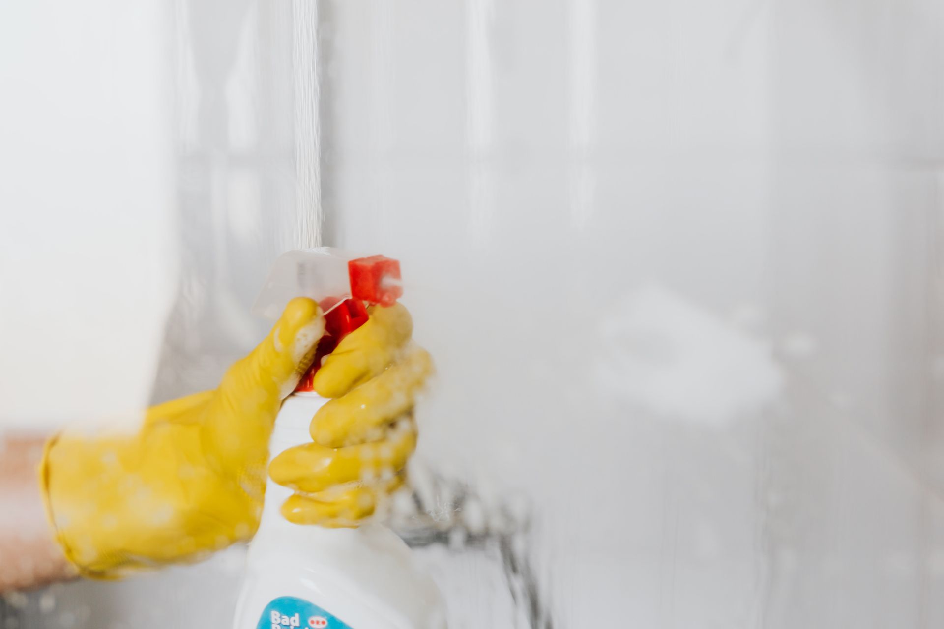 Person with yellow gloves spraying  down shower doors - Cleaning Services in Darling Downs, QLD