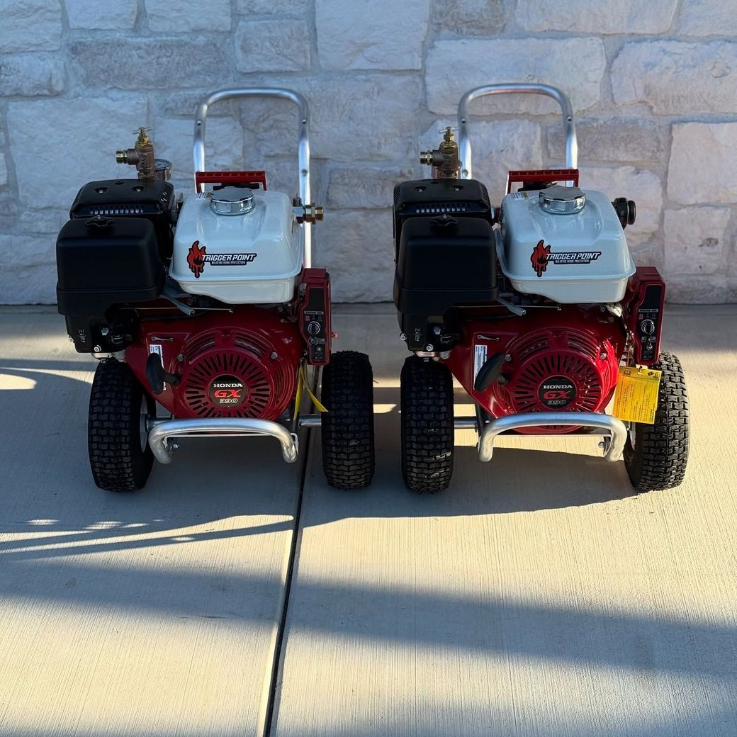 Two small red and black gas-powered machines parked side by side on a concrete surface against a stone wall.