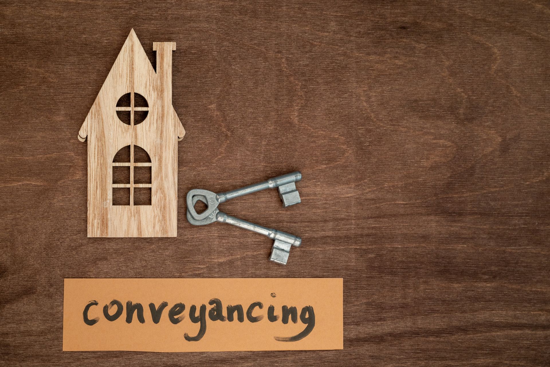 Cut-out wooden house with a key and a card saying 'conveyancing' on a wooden background.