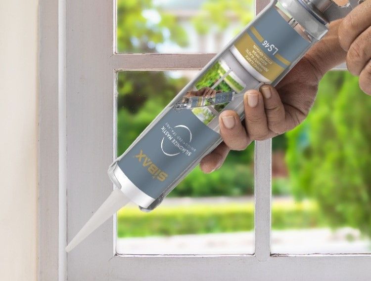 A person is holding a bottle of sealant and applying it to a window.