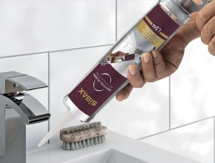A person is holding a bottle of silicone sealant over a sink