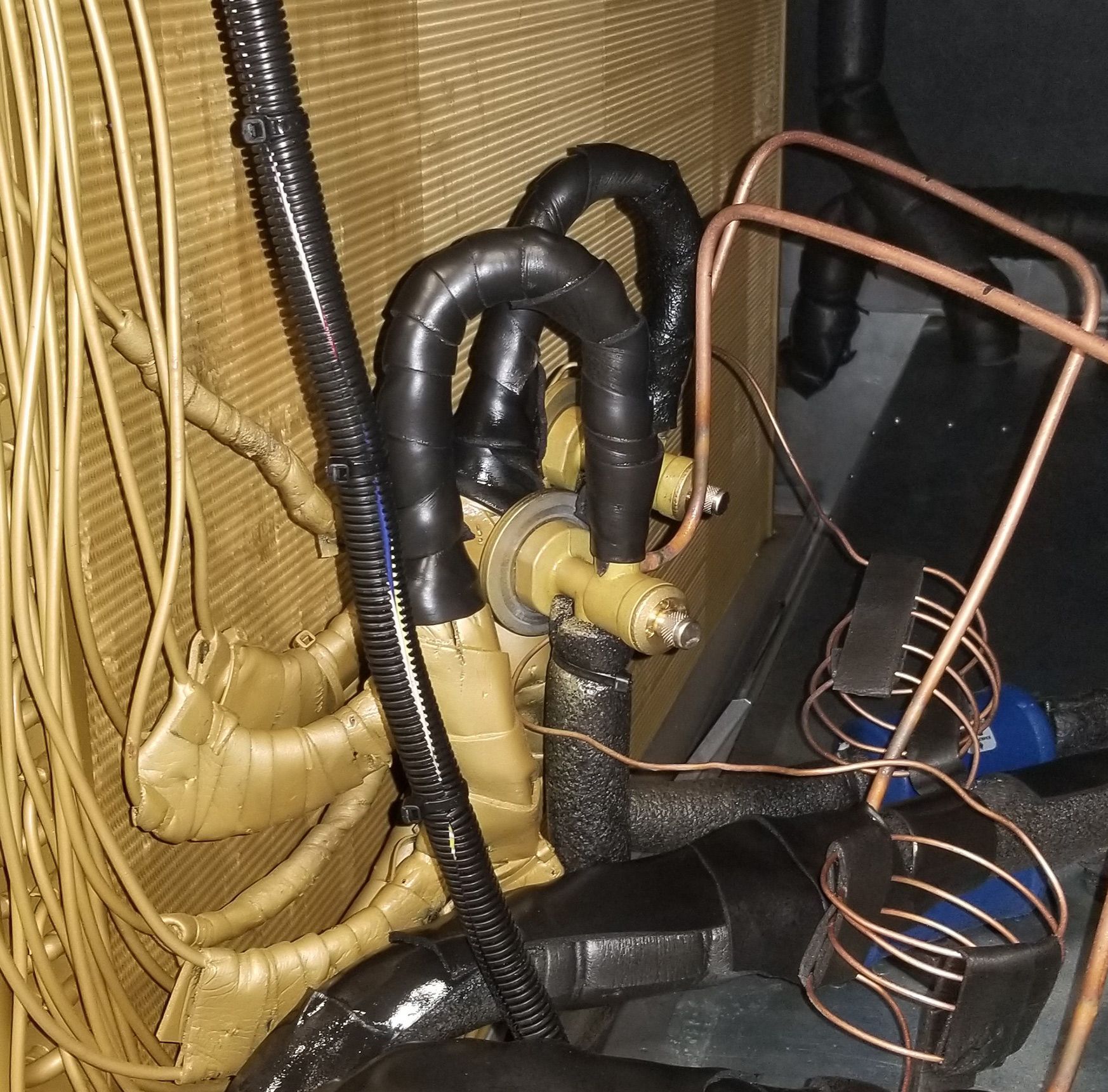 Close-up of insulated copper pipes and wiring inside an HVAC unit, with black tape and coils visible.