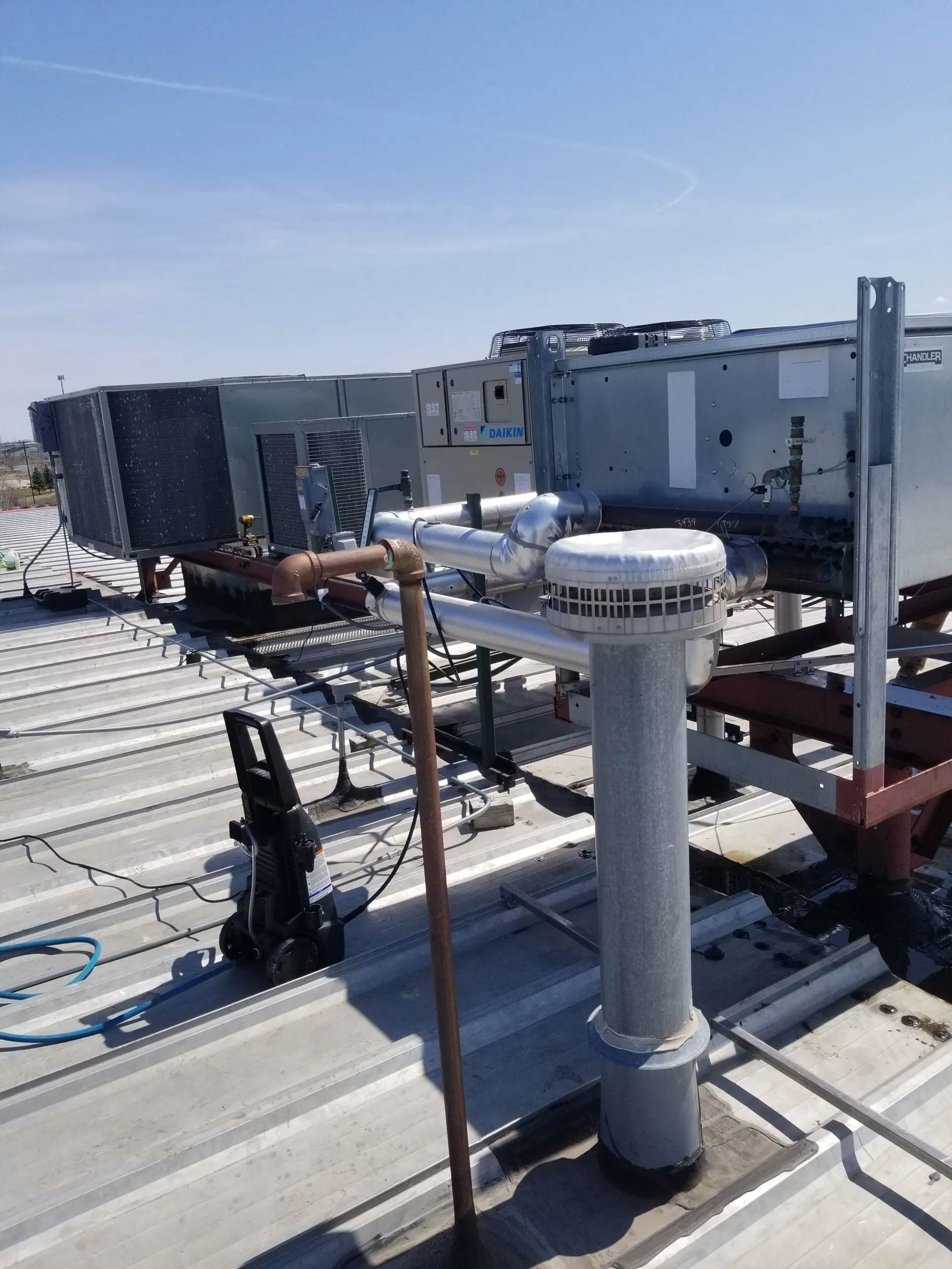 Rooftop HVAC units and white vent pipes on a sunlit industrial roof under a clear sky