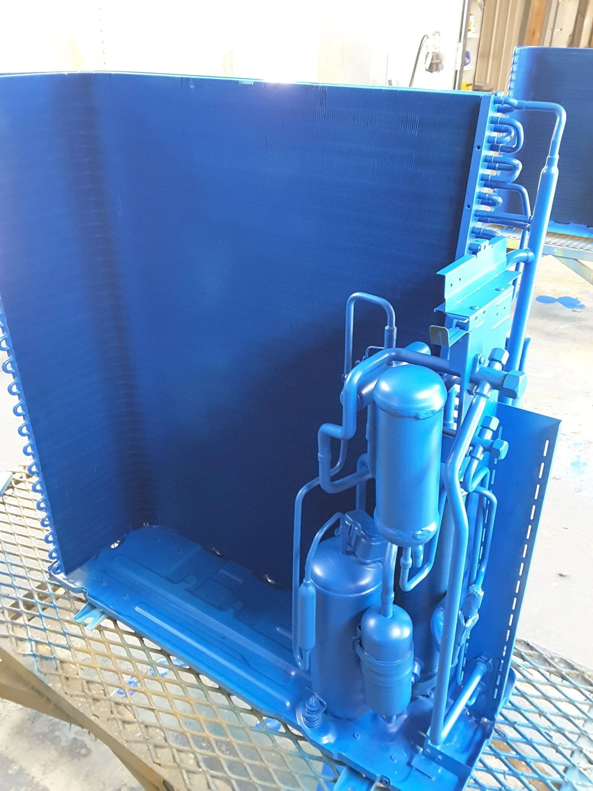 Blue industrial machinery in a metal enclosure, with a large blue tank and pipes on a grated floor.