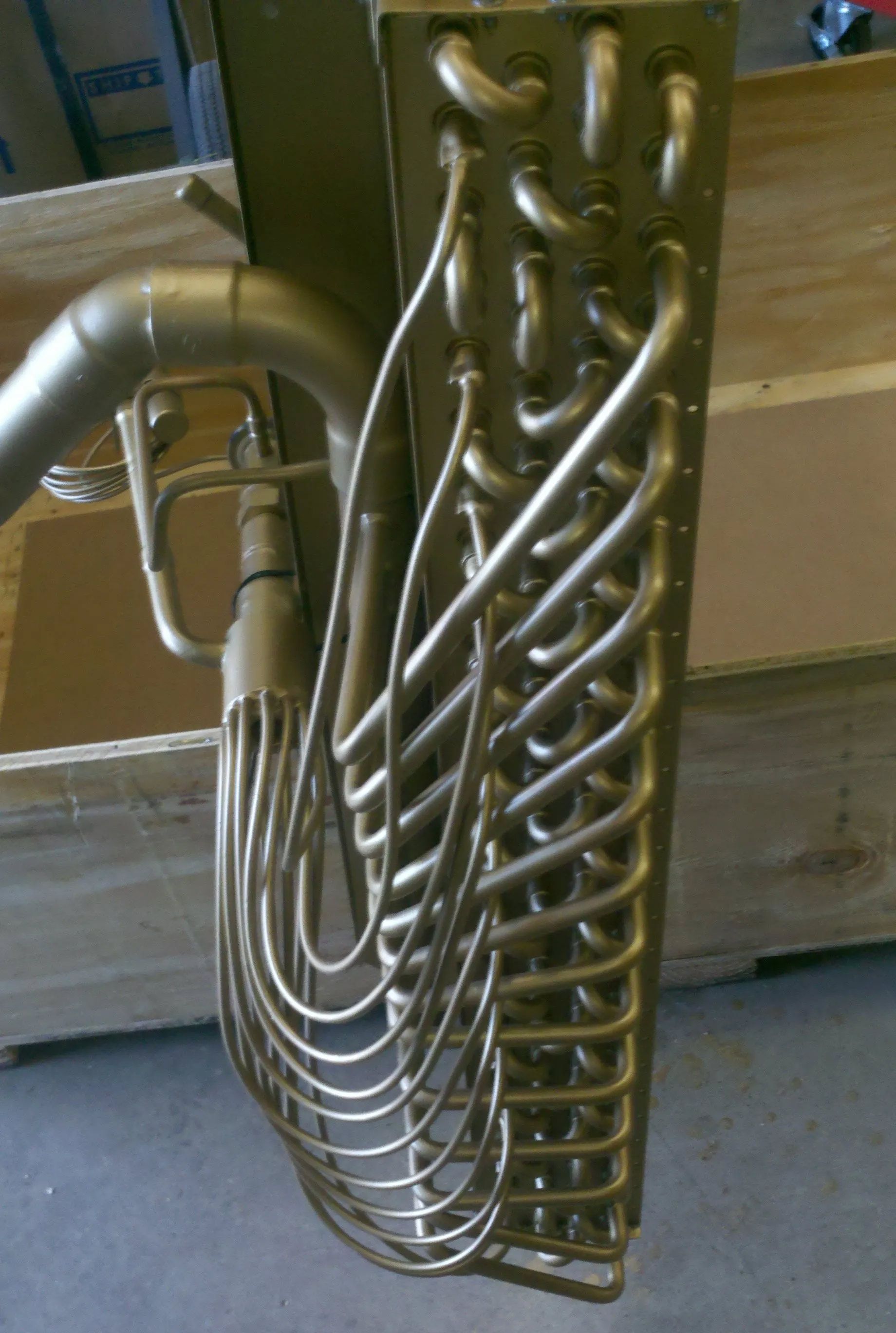Brass tuba coiled tubing and valves leaning against a wooden wall on a floor