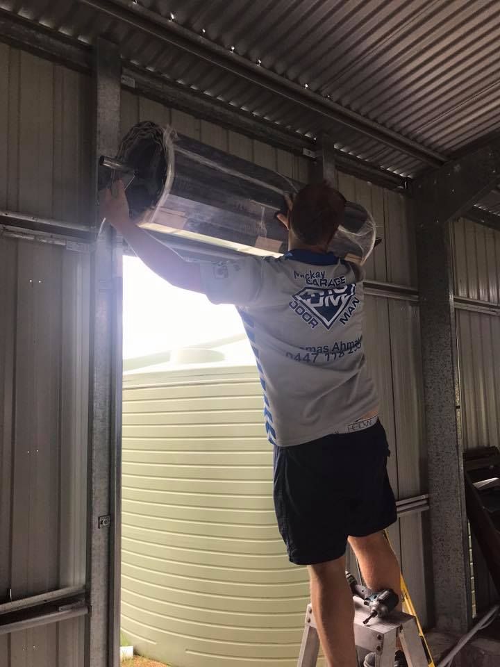 A Man is Standing on a Ladder Holding a Roll of Insulation — Mackay Garage Doors in Andergrove, QLD