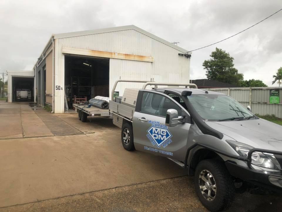 A Truck With a Trailer Attached to It is Parked in Front of a Building — Mackay Garage Doors in Andergrove, QLD