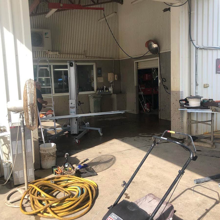 A Lawn Mower is Parked in a Garage Next to a Hose — Mackay Garage Doors in Andergrove, QLD