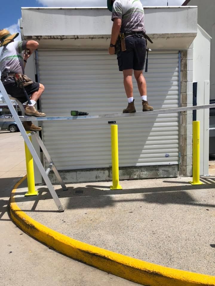 Two Men Are Working on a Garage Door in a Parking Lot — Mackay Garage Doors in Andergrove, QLD