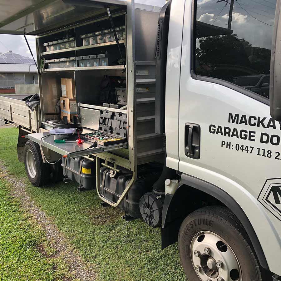A White Truck With the Word Mackay Garage on the Side is Parked in the Grass — Mackay Garage Doors in Andergrove, QLD