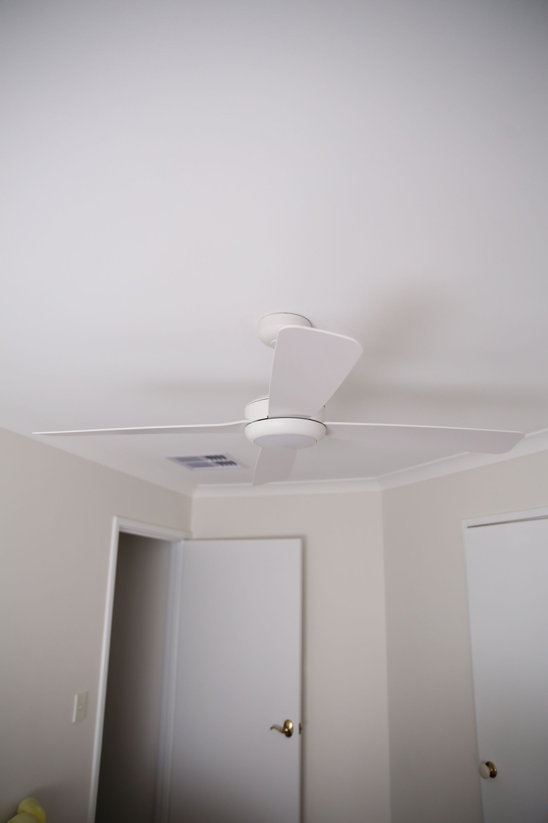 Ceiling fan in a beige room with two white doors and a dark doorway on the left.