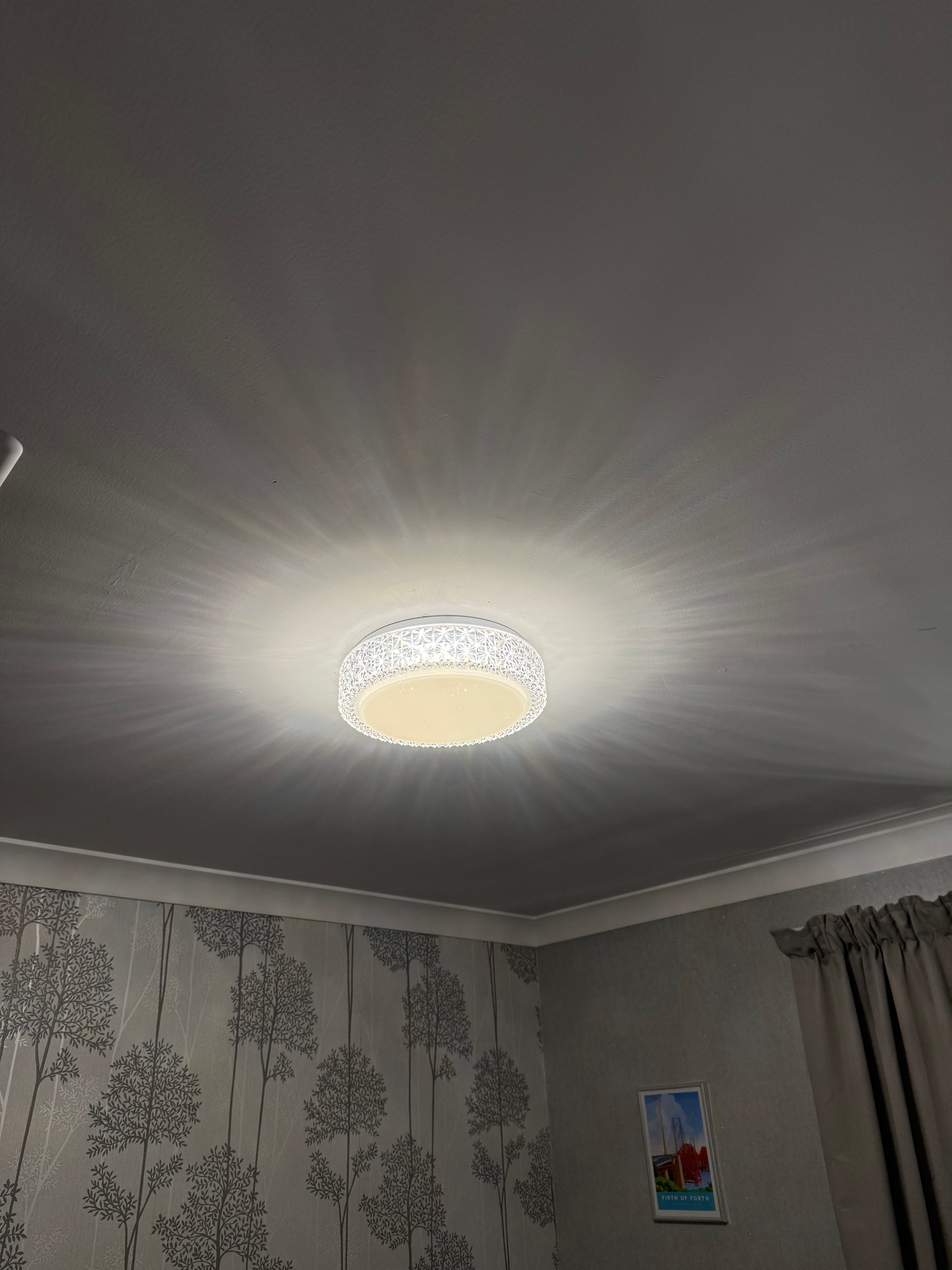 Ceiling light glowing in a room with patterned wallpaper and gray curtains.