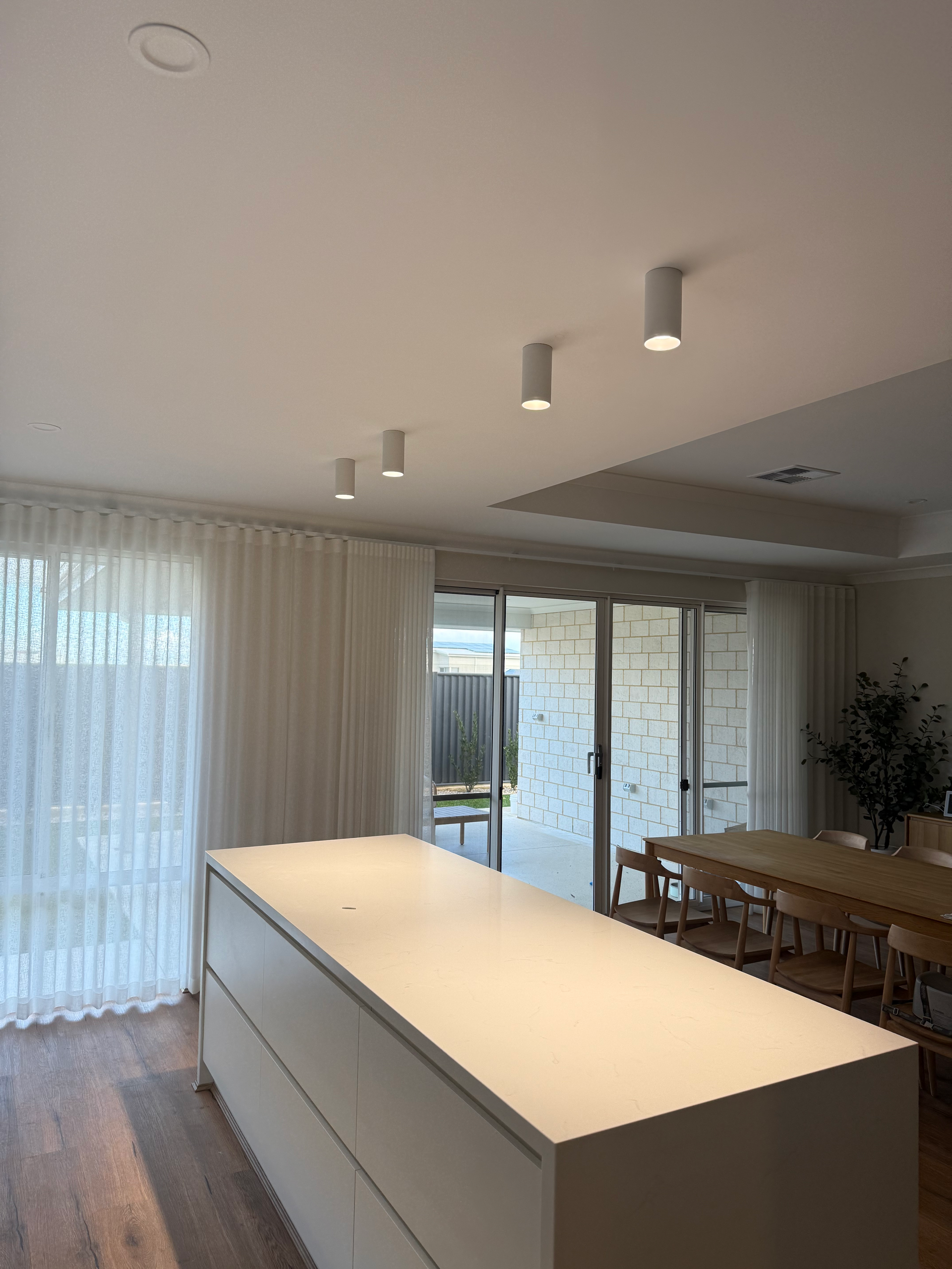 Modern open-plan dining area with white island, wood floors, large windows, and pendant lights