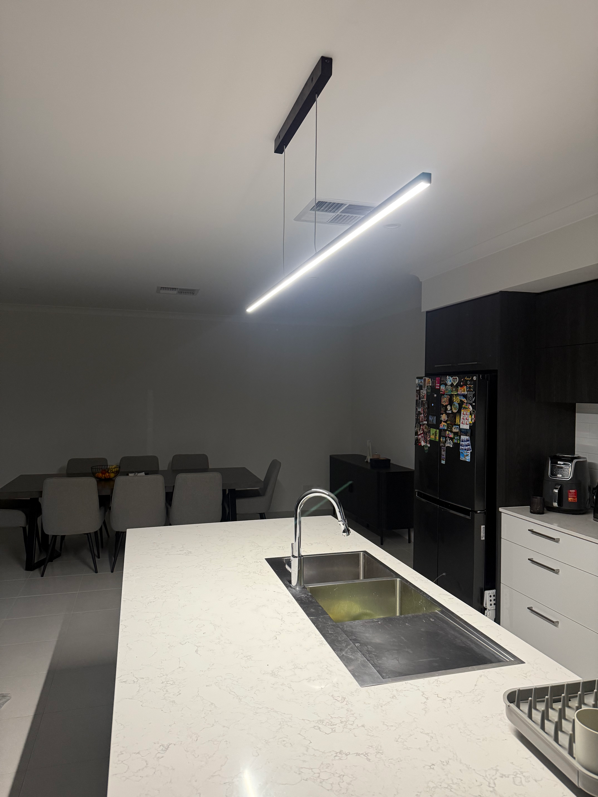 Modern kitchen with island sink, pendant light, and dining area in the background