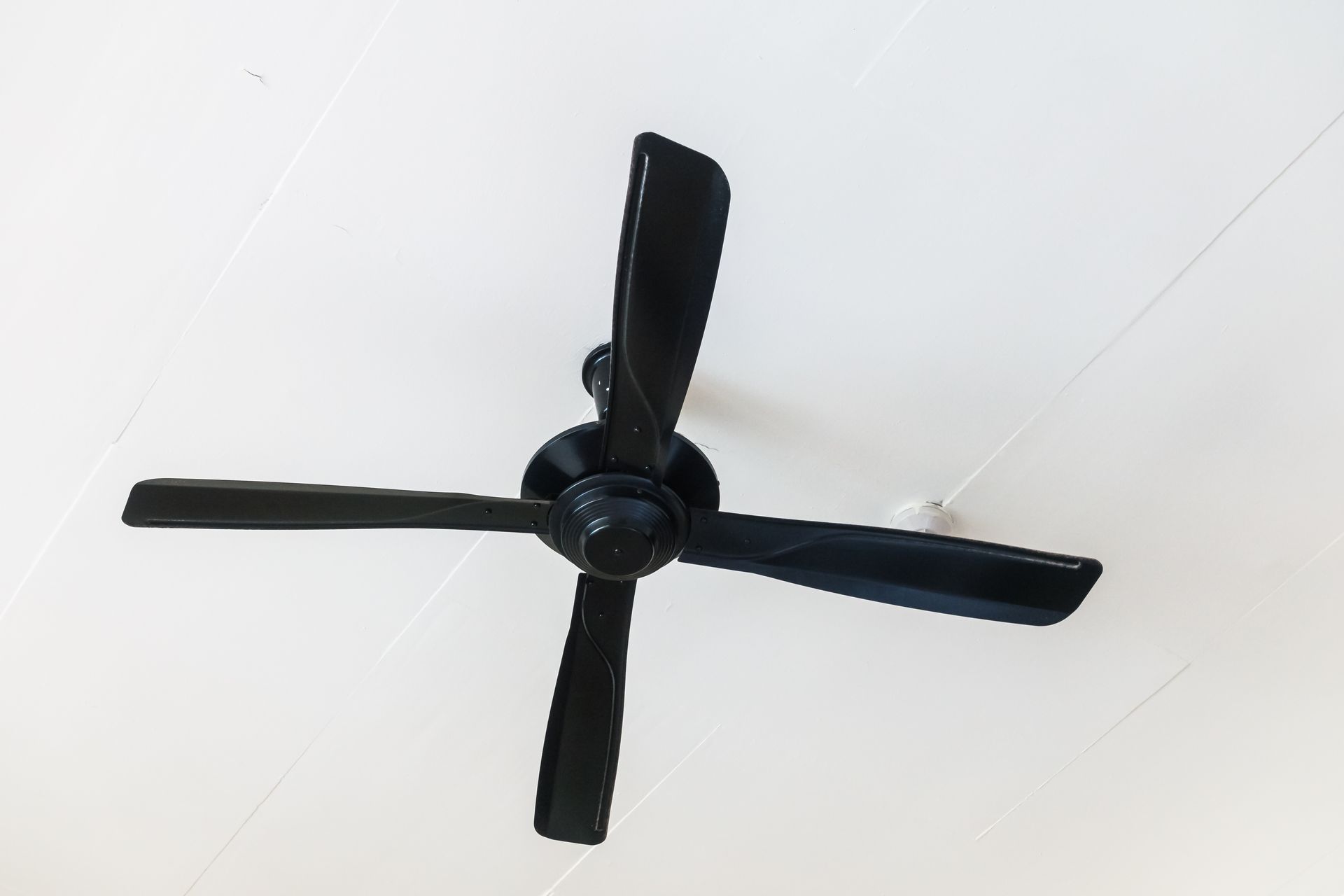 Black ceiling fan with four blades on a white ceiling, viewed from below