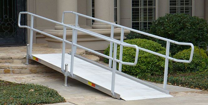 Aluminum wheelchair ramp with handrails leading up to a building entrance.