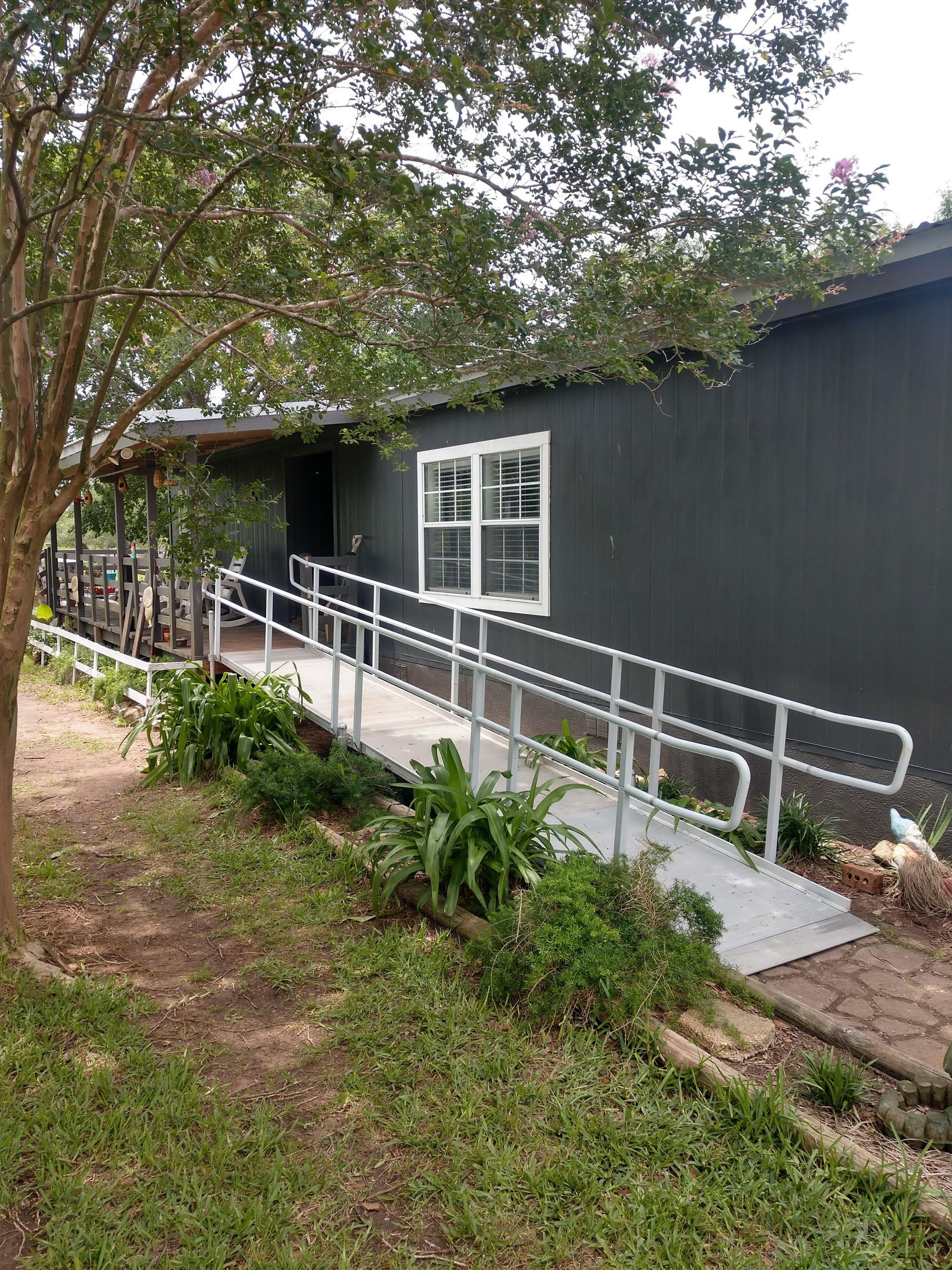 Gray building with a wheelchair ramp, surrounded by greenery, under a cloudy sky.