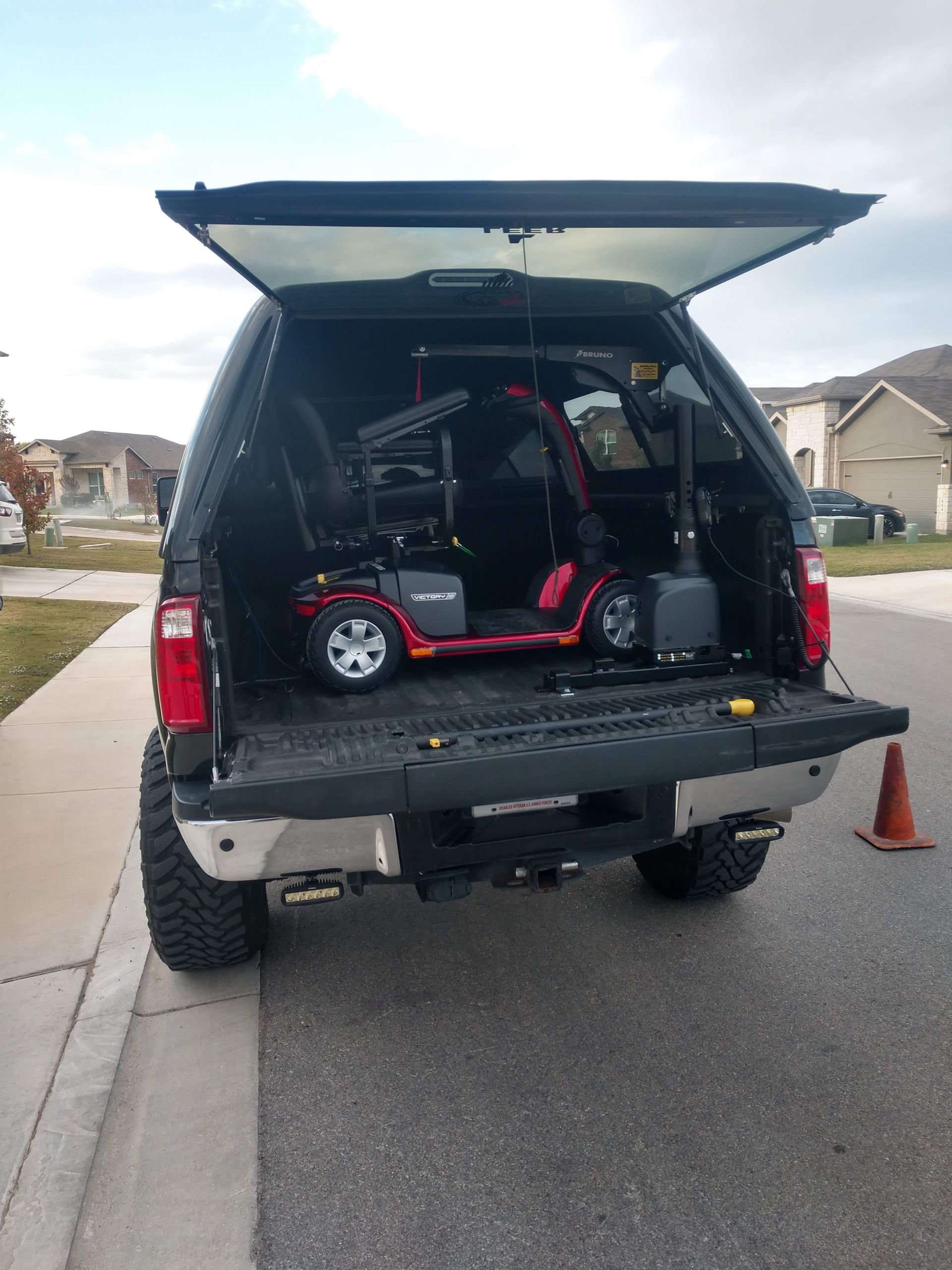 Red mobility scooter inside a truck bed with the tailgate down, parked on a street.