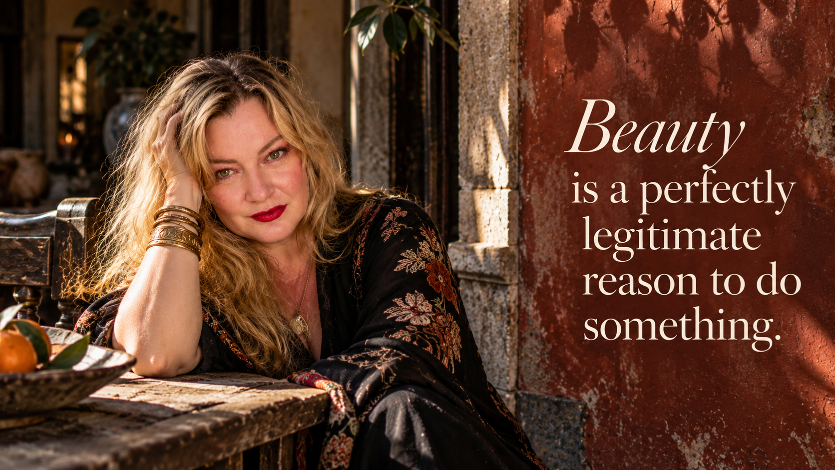 Lisa Hayes, a blonde woman in an embroidered black dress, seated against a weathered terracotta wall