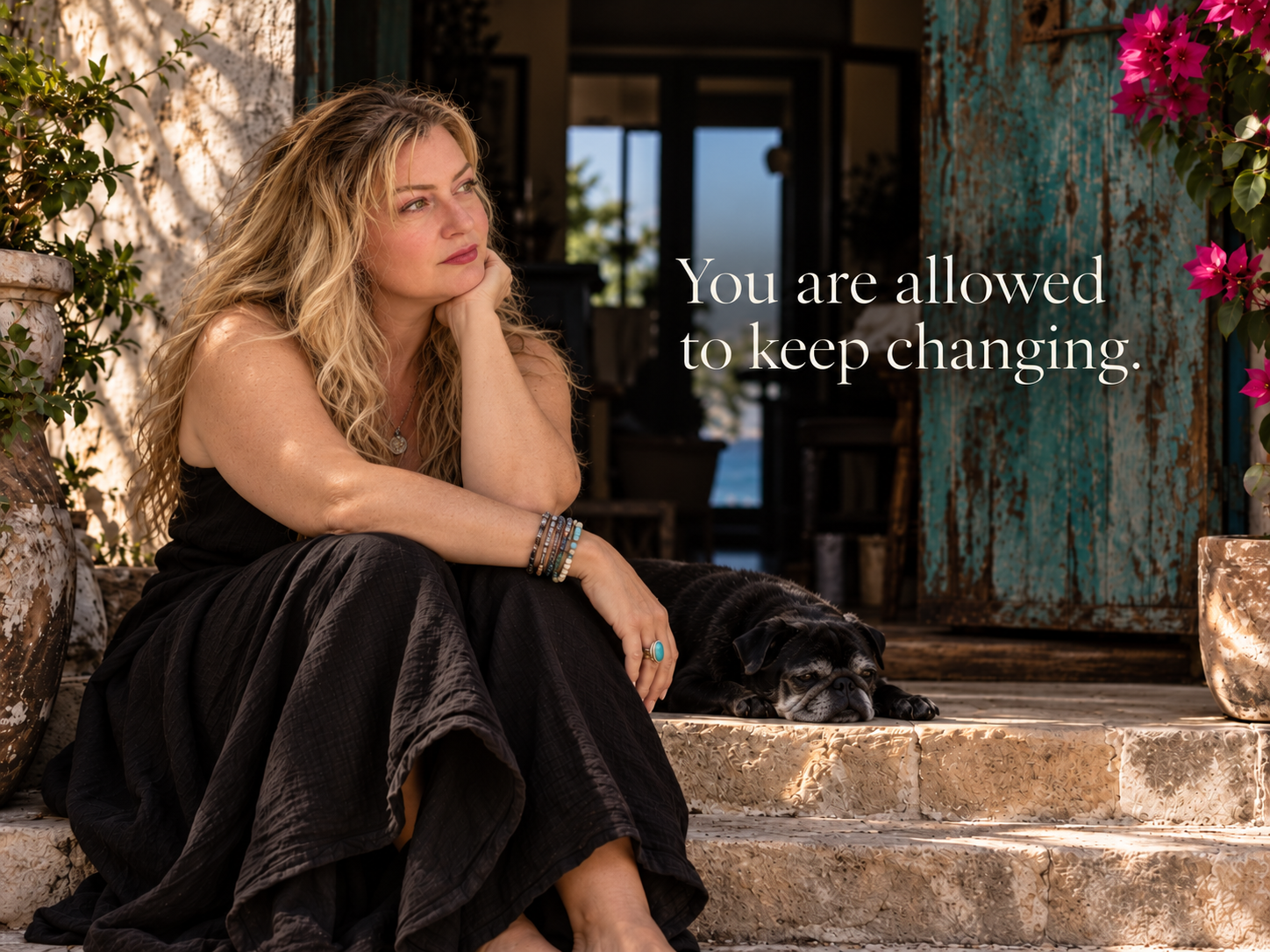A blonde woman in a flowing black dress sits thoughtfully on sunlit stone steps