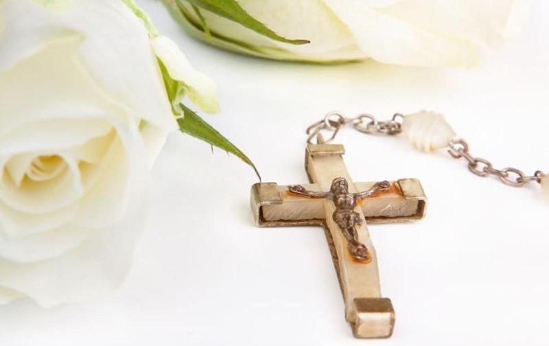 Collana con crocifisso in legno accanto a rose bianche su sfondo bianco