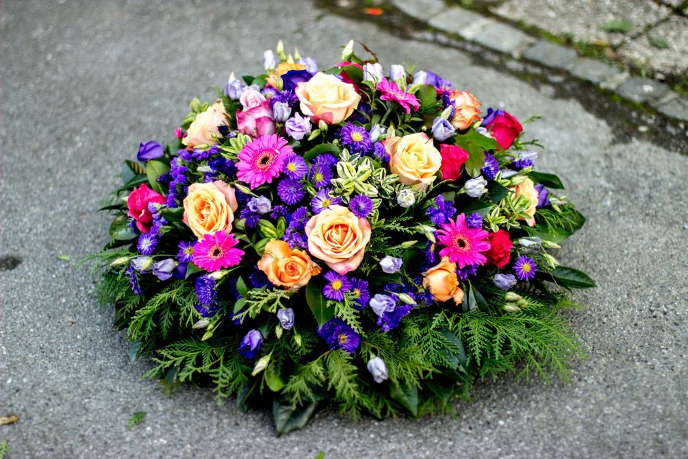 Composizione floreale colorata con fiori rosa, viola e color pesca su una superficie di pietra.