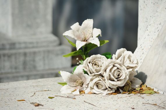 Rose bianche e un fiore bianco disposti su una sporgenza di pietra in un luogo commemorativo.