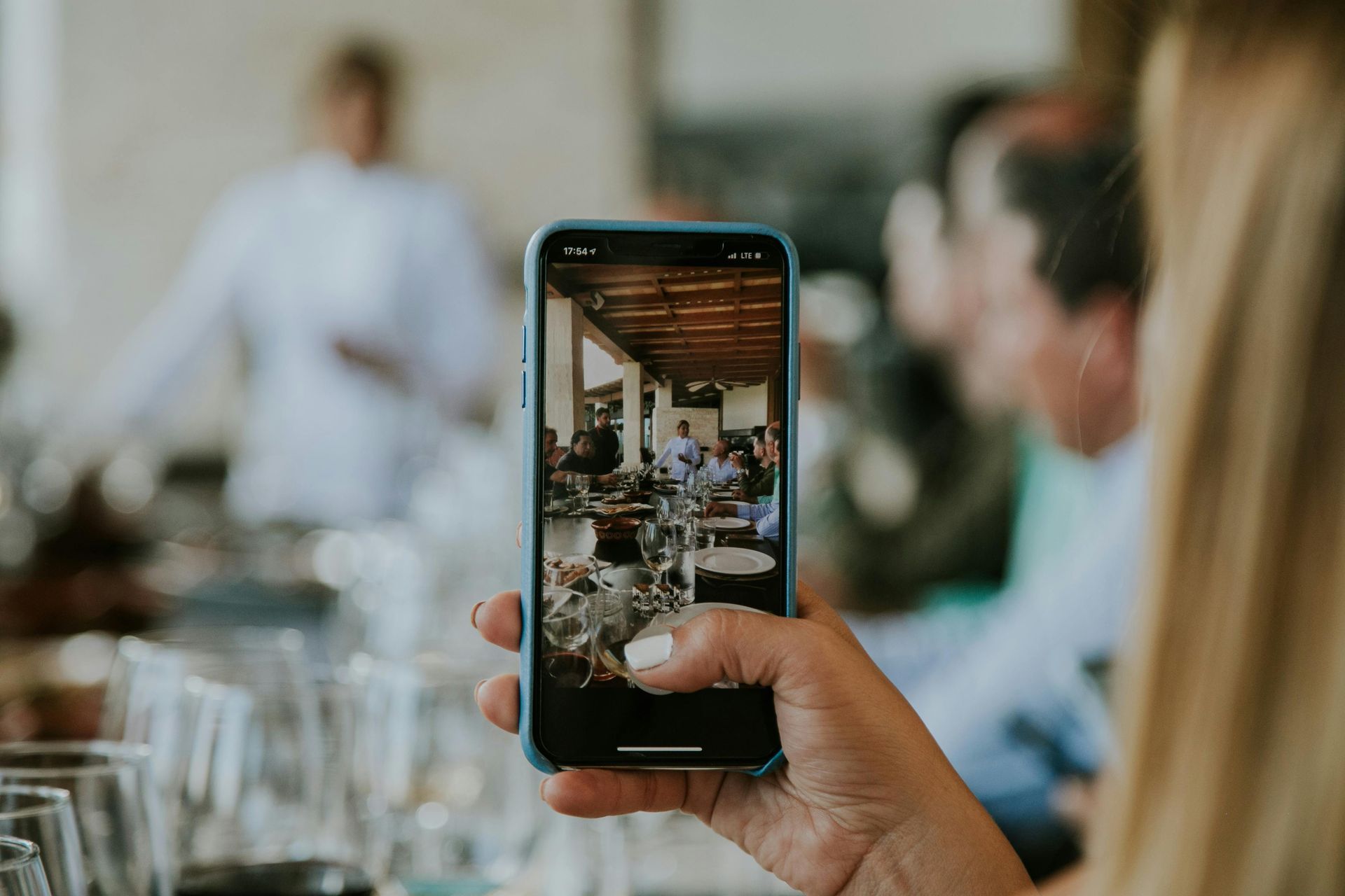 Person taking photo with phone, capturing restaurant scene with chef and patrons.
