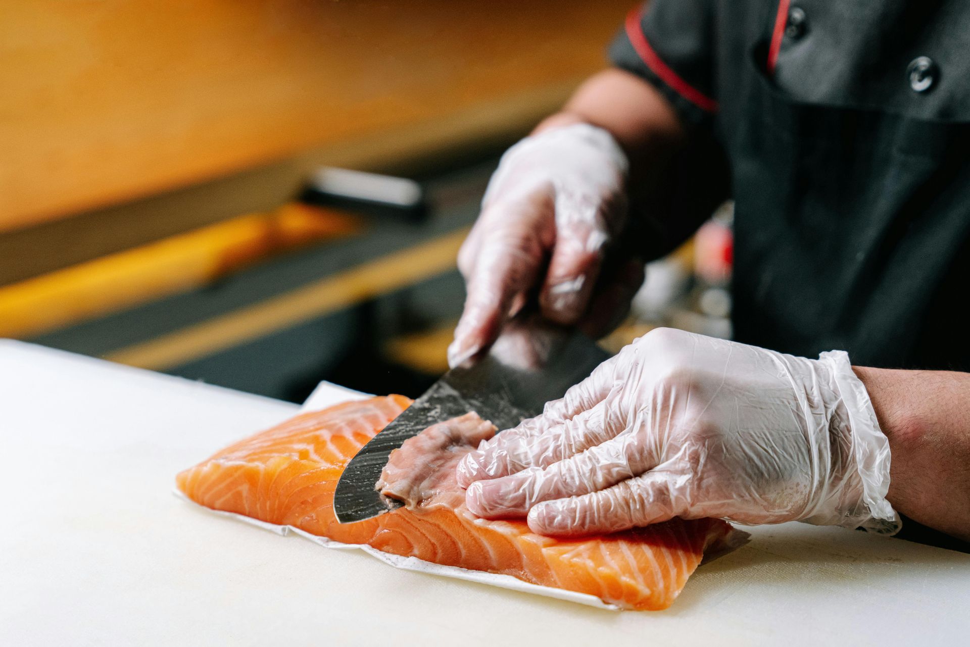 A person wearing gloves is cutting a piece of salmon on a cutting board.