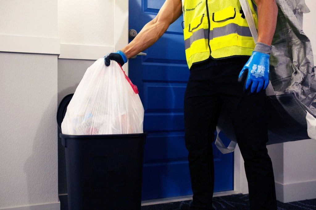 Employee in safety vest and gloves taking out trash.