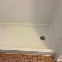 Empty shower stall with white walls, tiled floor, and a drain on the right side