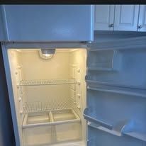 Open refrigerator with empty shelves and door bins, lit interior, white finish.