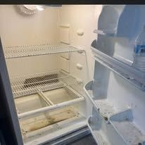 Empty white refrigerator interior with shelves and door bins, slightly dirty bottom shelf.