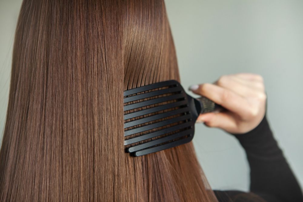 A woman is brushing her long brown hair with a black comb.