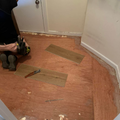 Person kneeling on a hardwood floor installing rectangular floor patches in a small room.