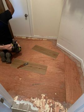 Partially stripped floor in a room, with exposed subfloor and tools at the left edge.