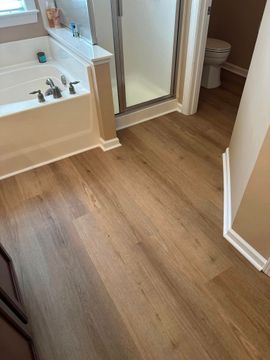 Bathroom with wood-look flooring, a bathtub on the left, and a toilet visible through the doorway.