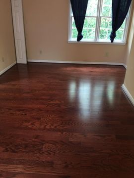 Empty room with dark wood floor, beige walls, and a window with black curtains.