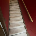 Carpeted staircase in a narrow hallway with red walls and a wooden handrail