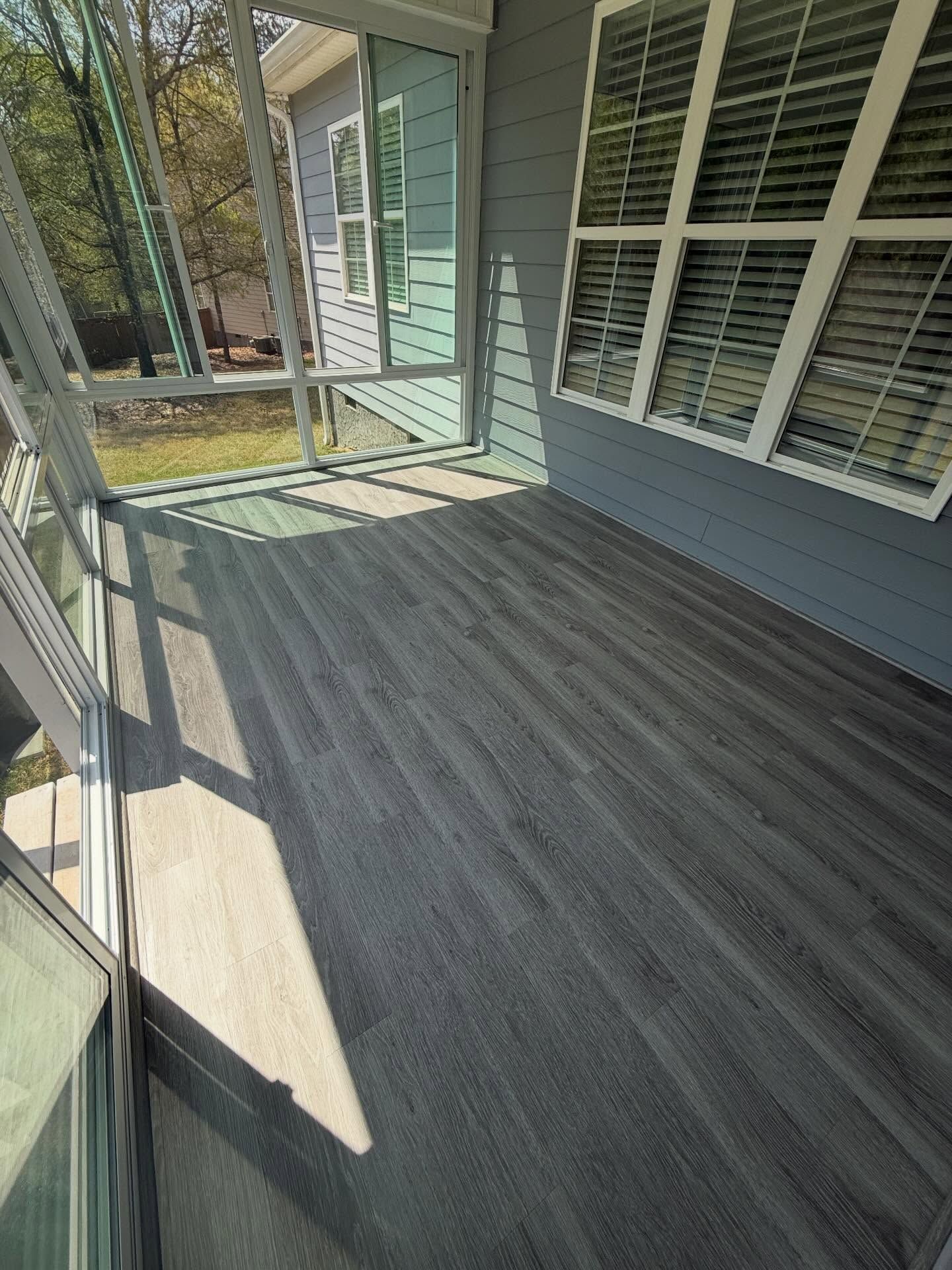 Covered porch with gray wood-look flooring, white siding, and large windows overlooking trees