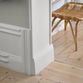 White interior doorway and wall trim beside a wicker chair on a light wood floor.