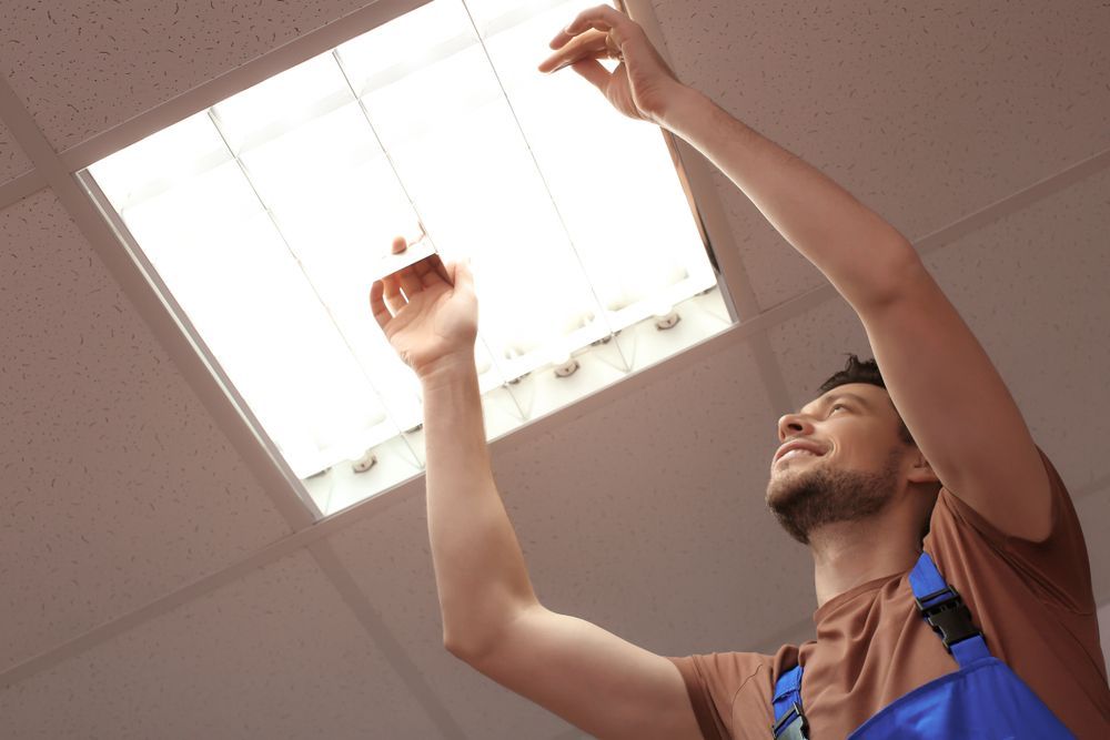 Man Reaching Into a Ceiling Light Fixture, Smiling, in a Room — Holders Electrical In Tenterfield, NSW